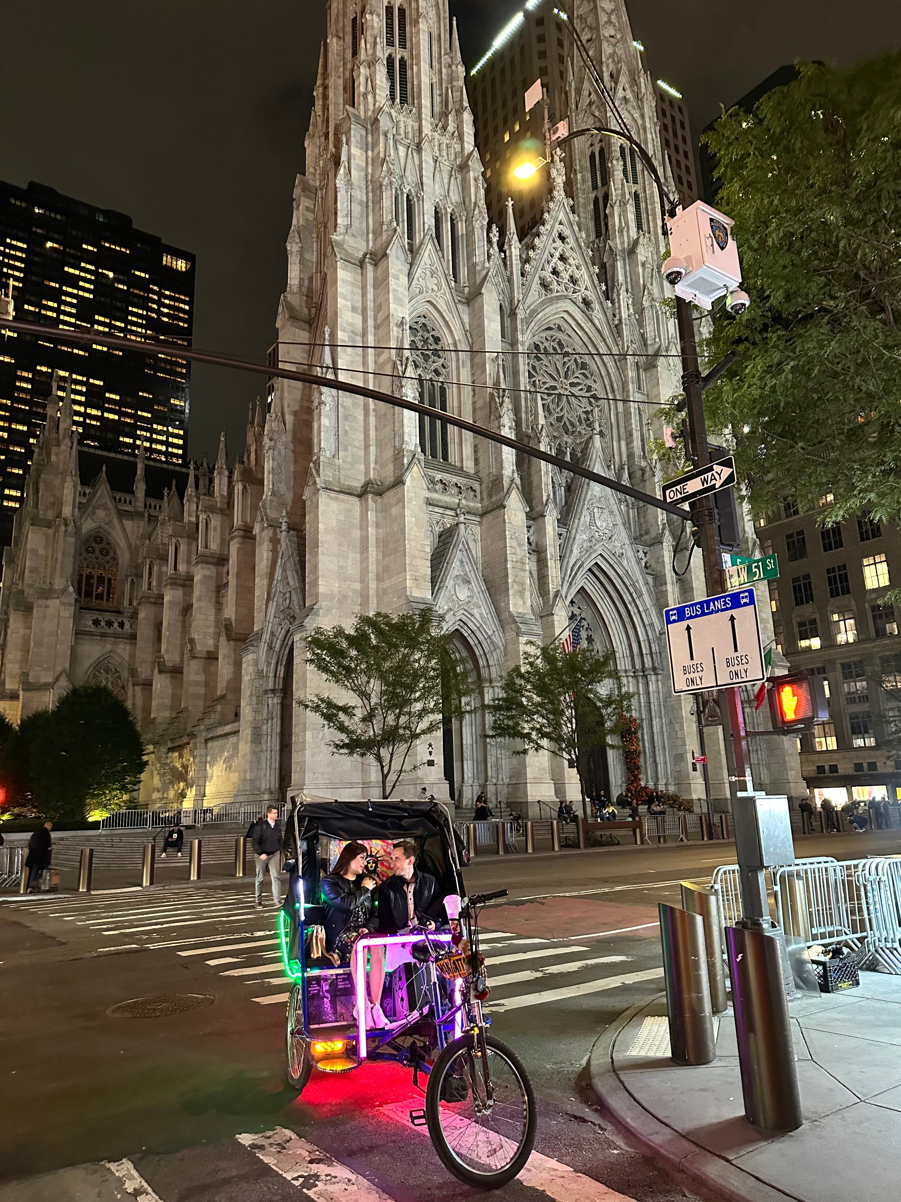 St. Patrick's Cathedral's ornate Gothic facade at night with a colorful neon-lit pedicab.