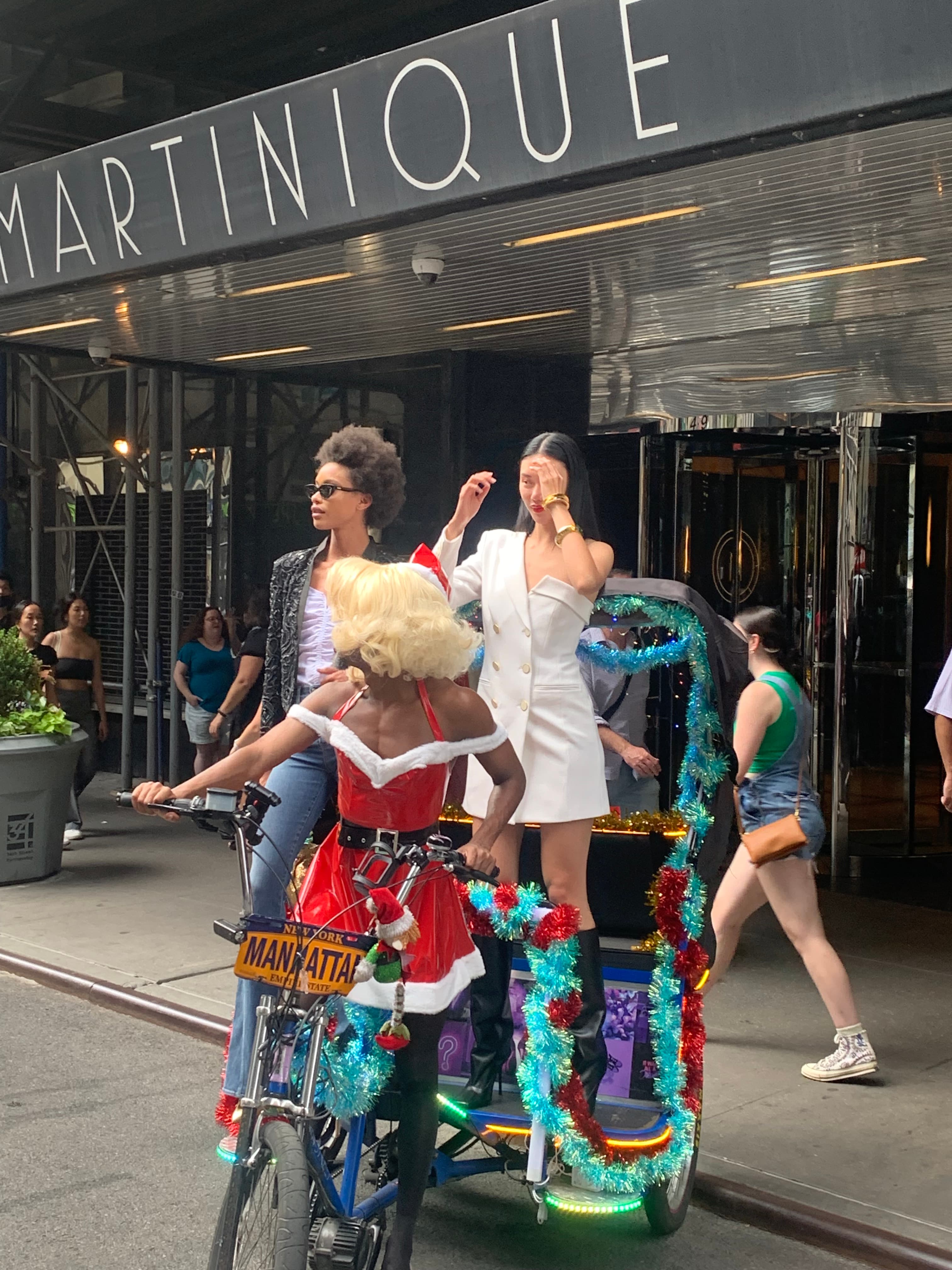 People in festive outfits pose with a tinsel-decorated pedicab outside the Martinique in Manhattan.